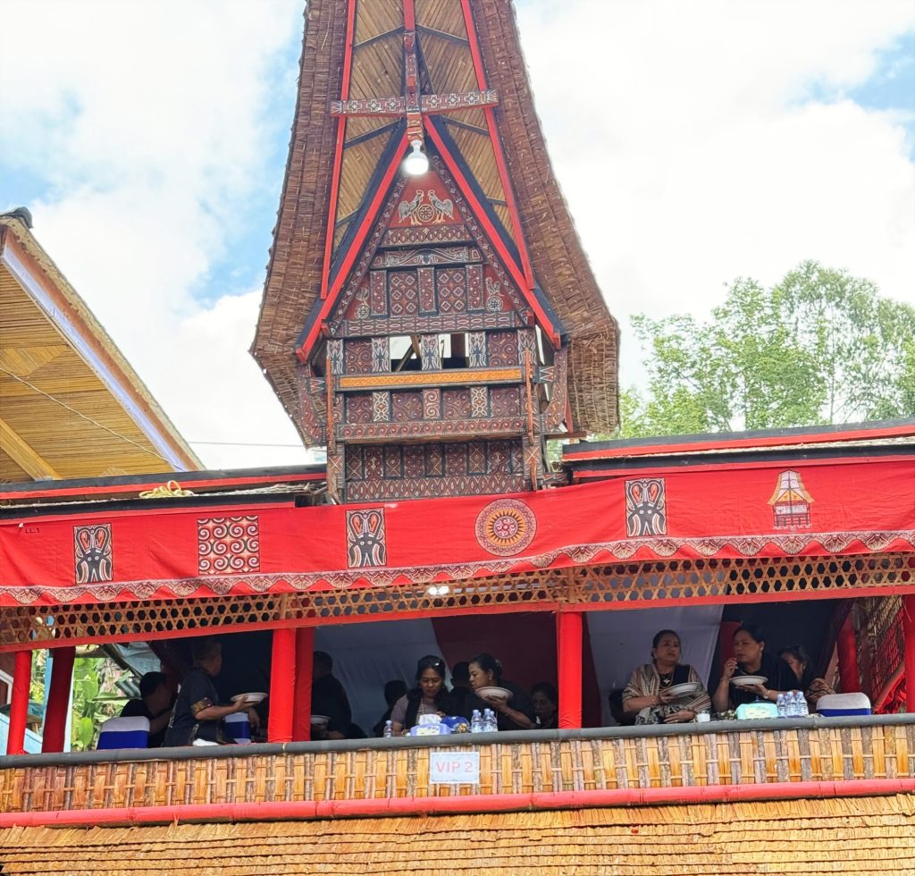 VIP section of a temporary tongkonan house built for Berta Bira's Rambu Solo funeral ceremony in Tana Toraja, Indonesia, with traditional carved panels and guests seated above