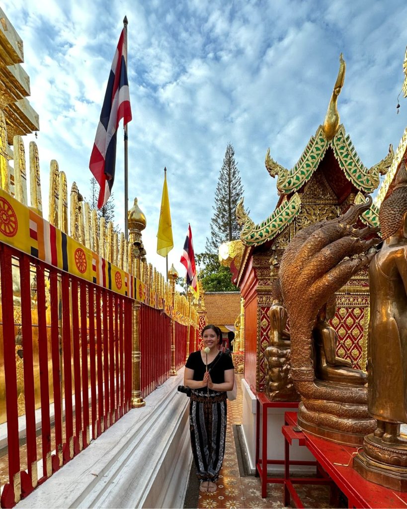 A female traveler holding a white lotus flower while participating in a traditional Buddhist prayer ritual at Doi Suthep temple.